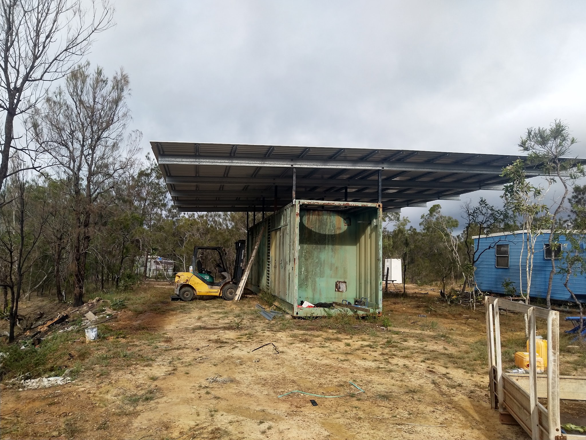 Finished skillion roof shelter built over a shipping container in bushland, with a forklift on site