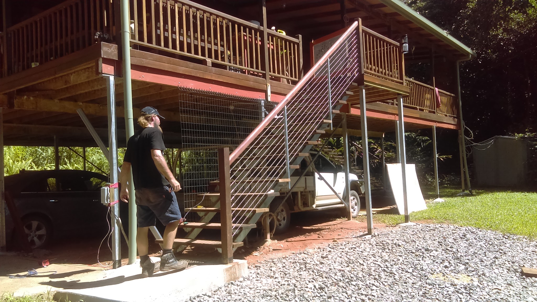 A steel staircase with a horizontal wire balustrade fitted to a high set Queenslander, with a tradesman working underneath the deck