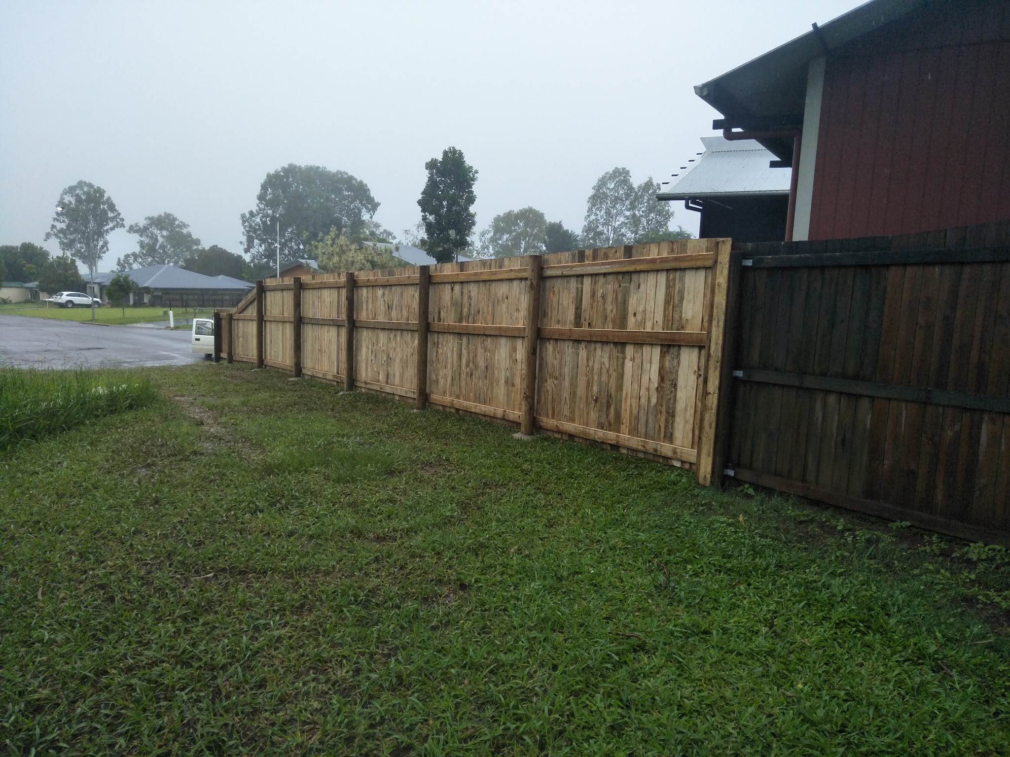 New hardwood paling fence on a suburban corner block, photographed in the rain
