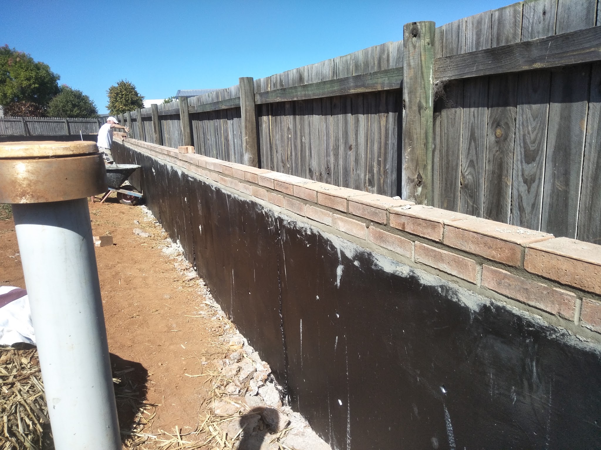 Rendered retaining wall with a brick capping being laid alongside an older timber paling fence